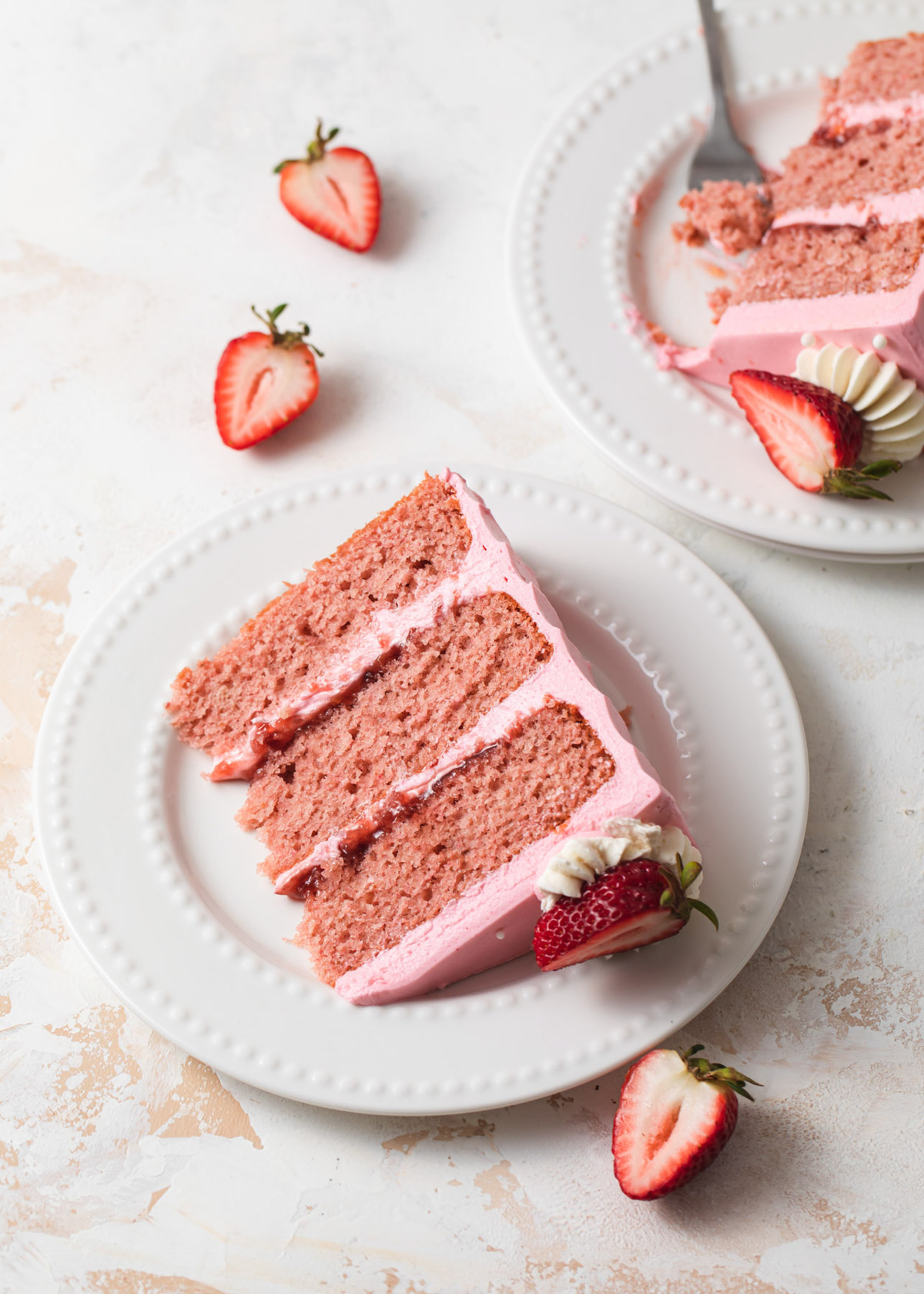 Two slices of pink strawberry cake with jam filling and pink frosting