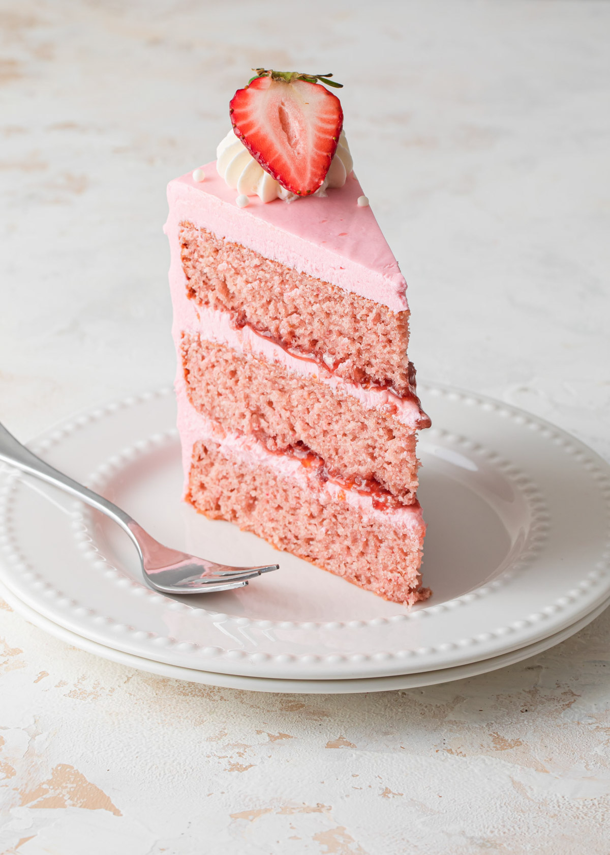 A slice of three-layer strawberry cake with jam filling and pink frosting