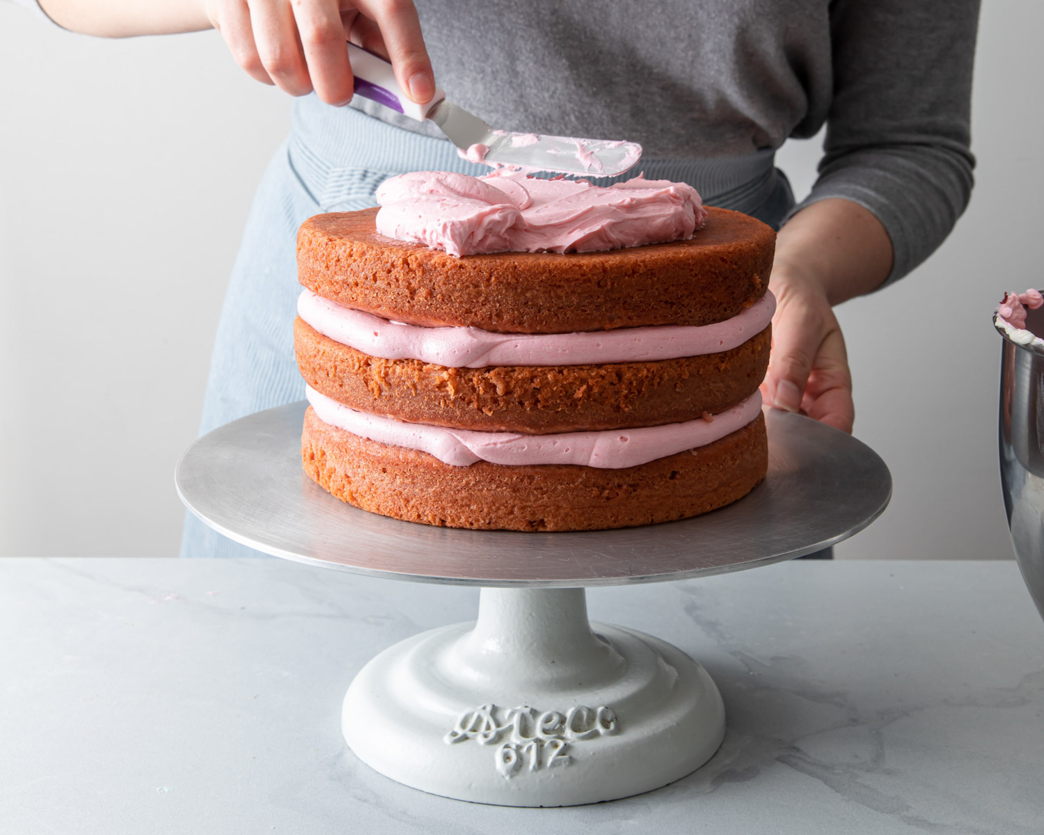 Frosting a three layer strawberry cake with pink buttercream
