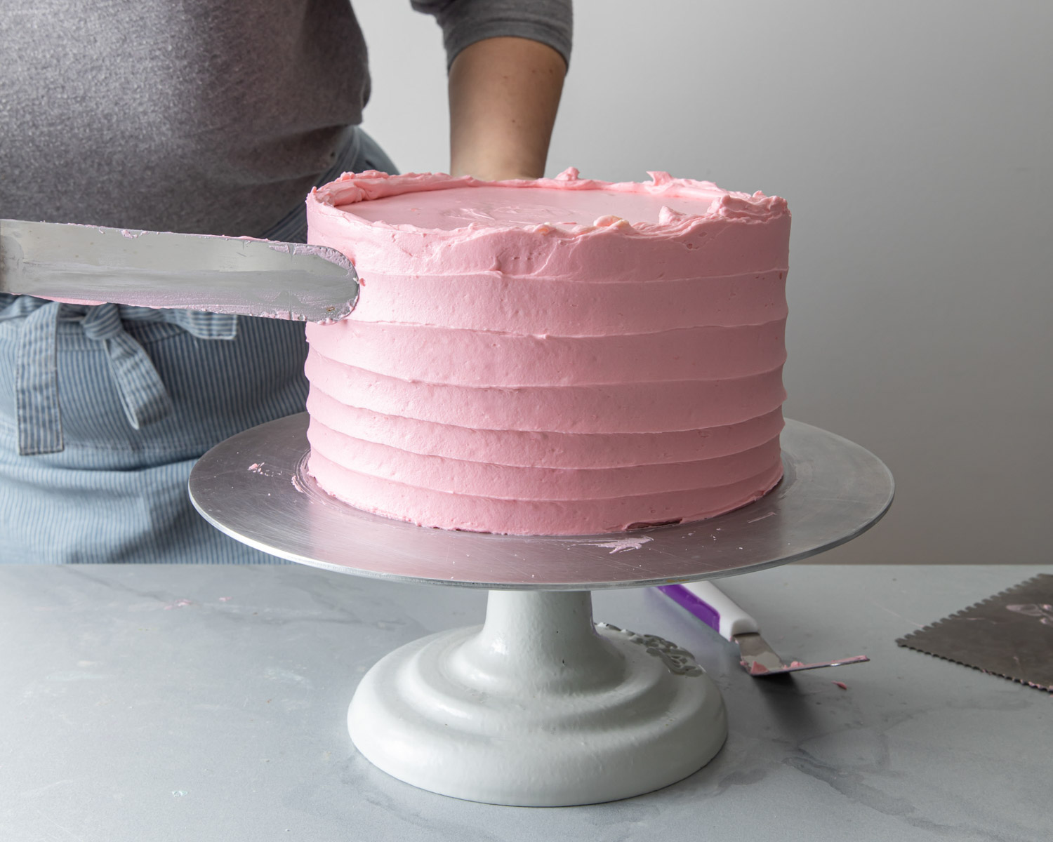 Frosting a pink cake with an offset spatula