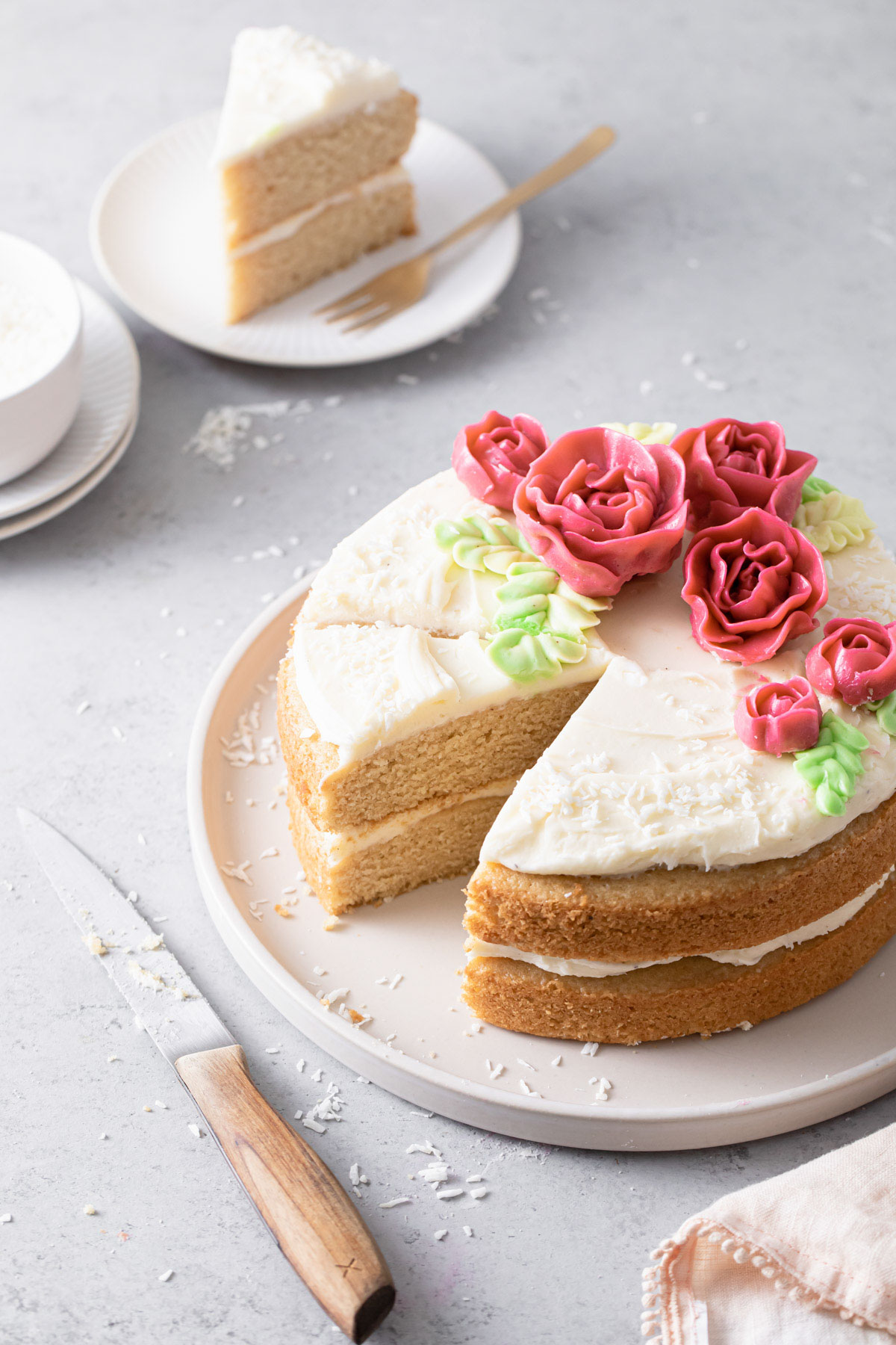 A two-layer almond cake with cream cheese frosting and pink buttercream roses on top that has been sliced