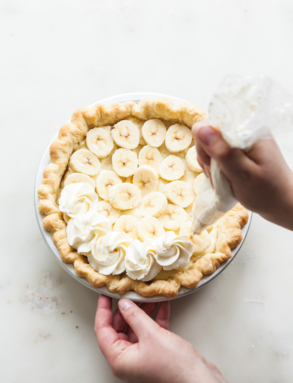 Piping whipped cream on top of a banana cream pie