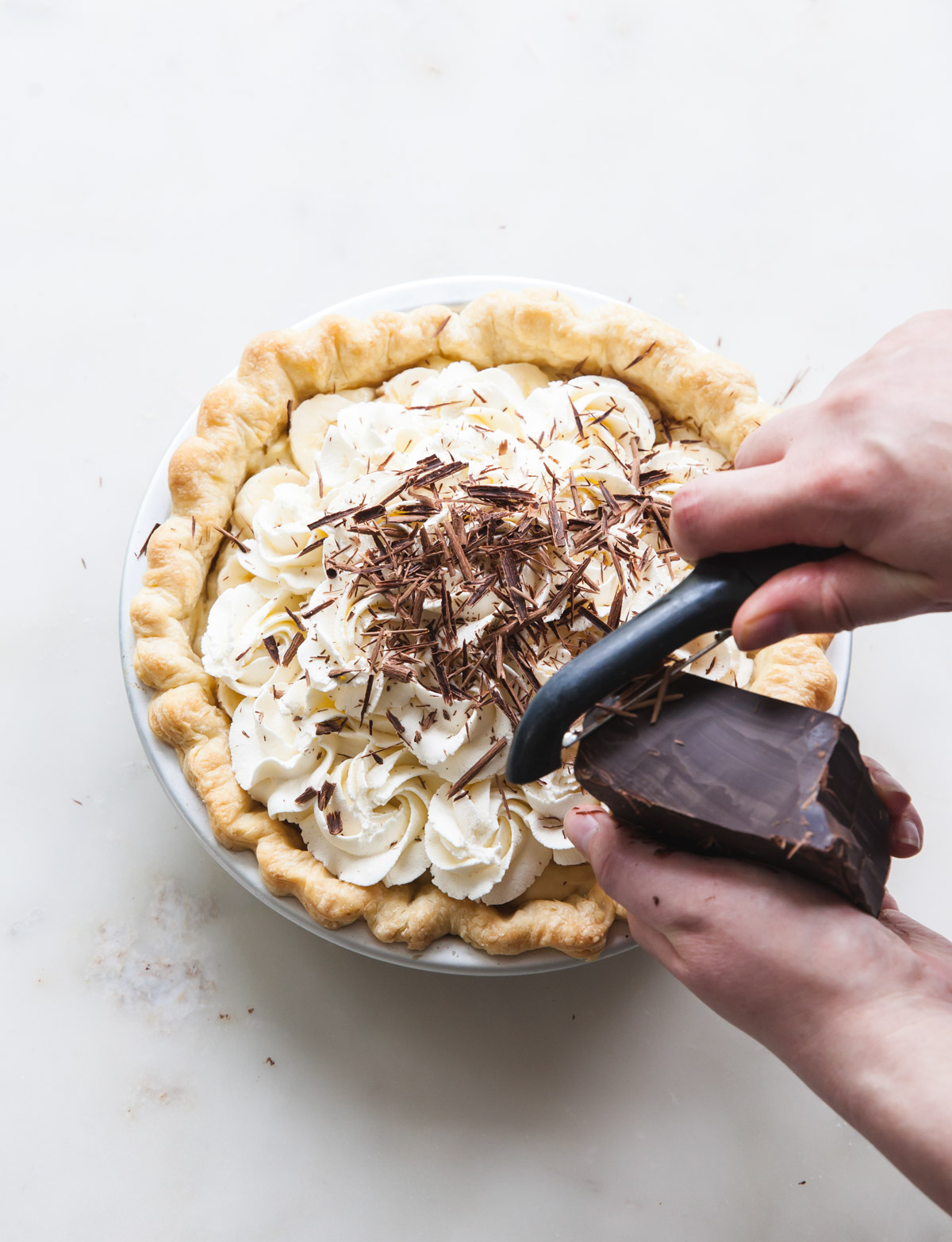 Chocolate shavings being grated on a banana cream pie