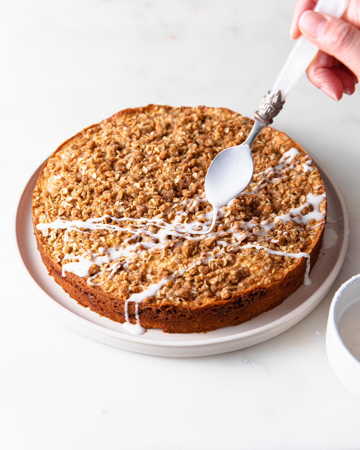 A spoon drizzling glaze on a carrot coffee cake