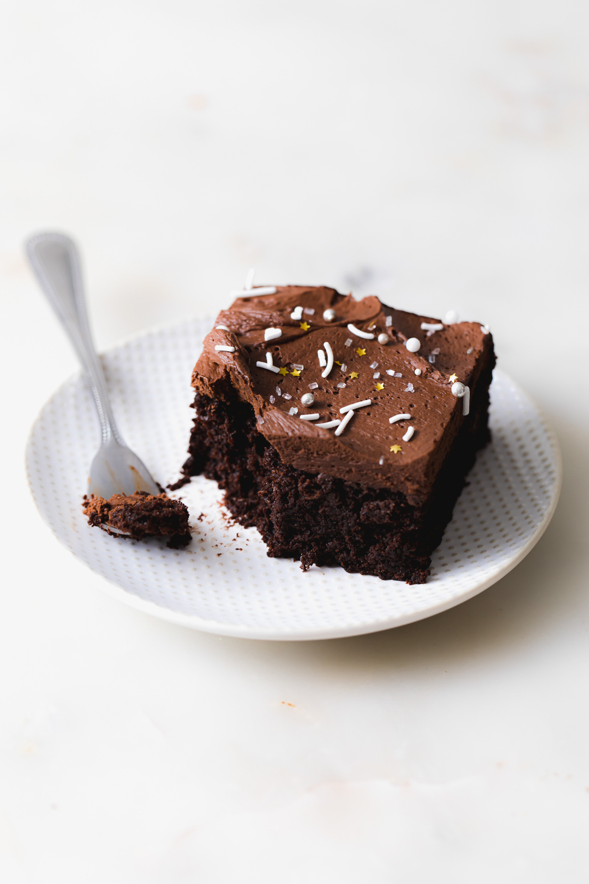 A slice of chocolate snack cake on a plate with whipped ganache frosting