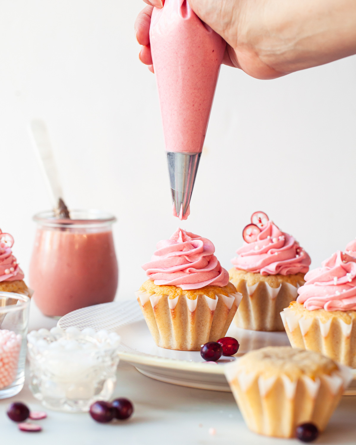 Cranberry cupcakes with pink cranberry frosting being piped on top