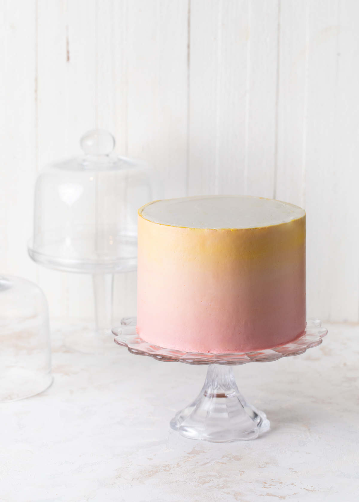 A pink to yellow buttercream ombre cake on a glass cake stand
