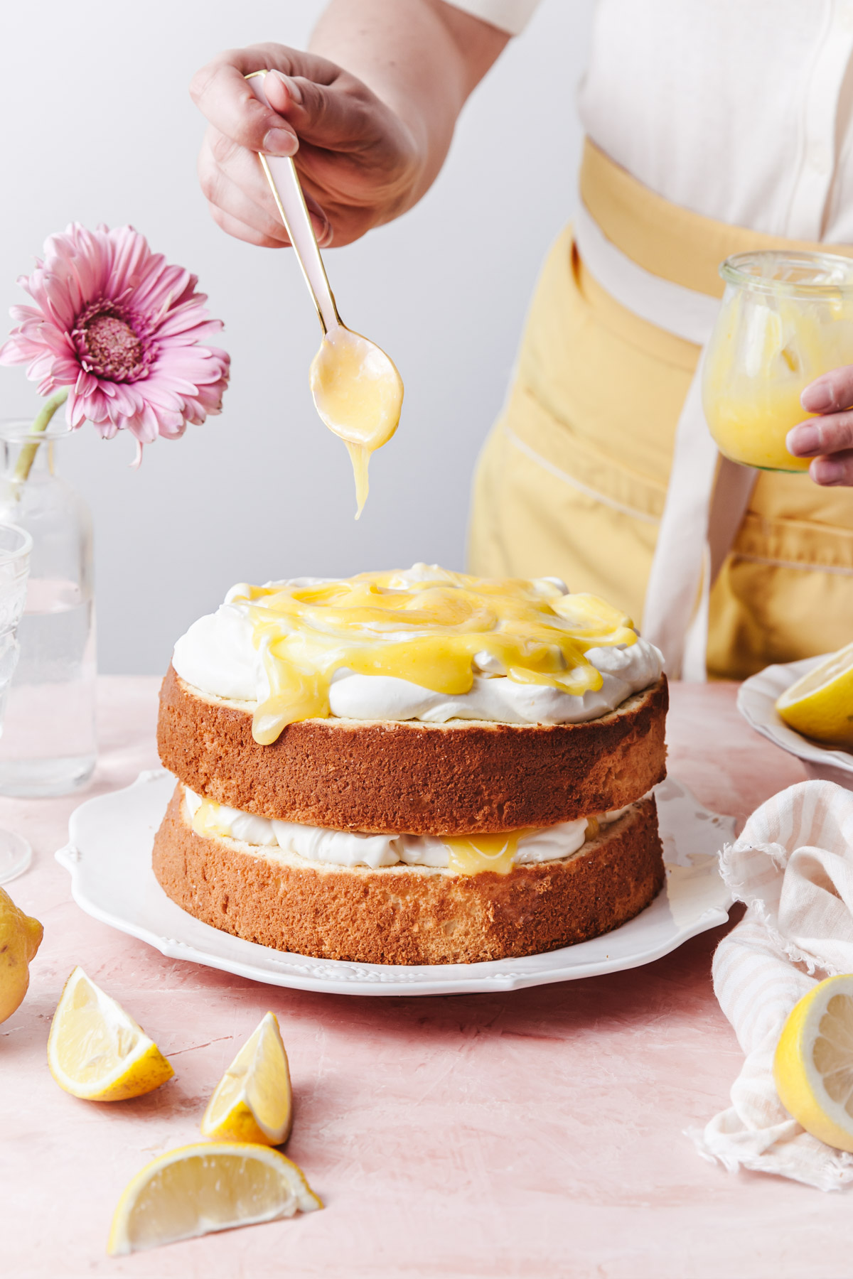 A two layer lemon chiffon cake with swirls of lemon curd being spooned on top