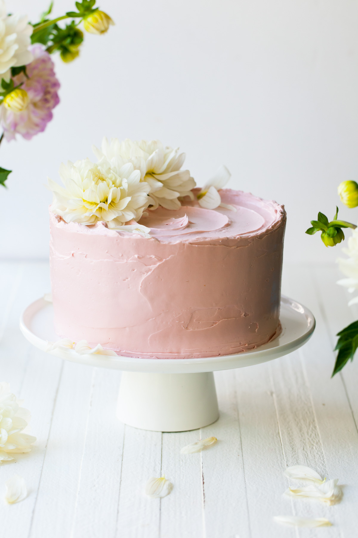 A pink French buttercream cake with white flowers on top of a white cake stand