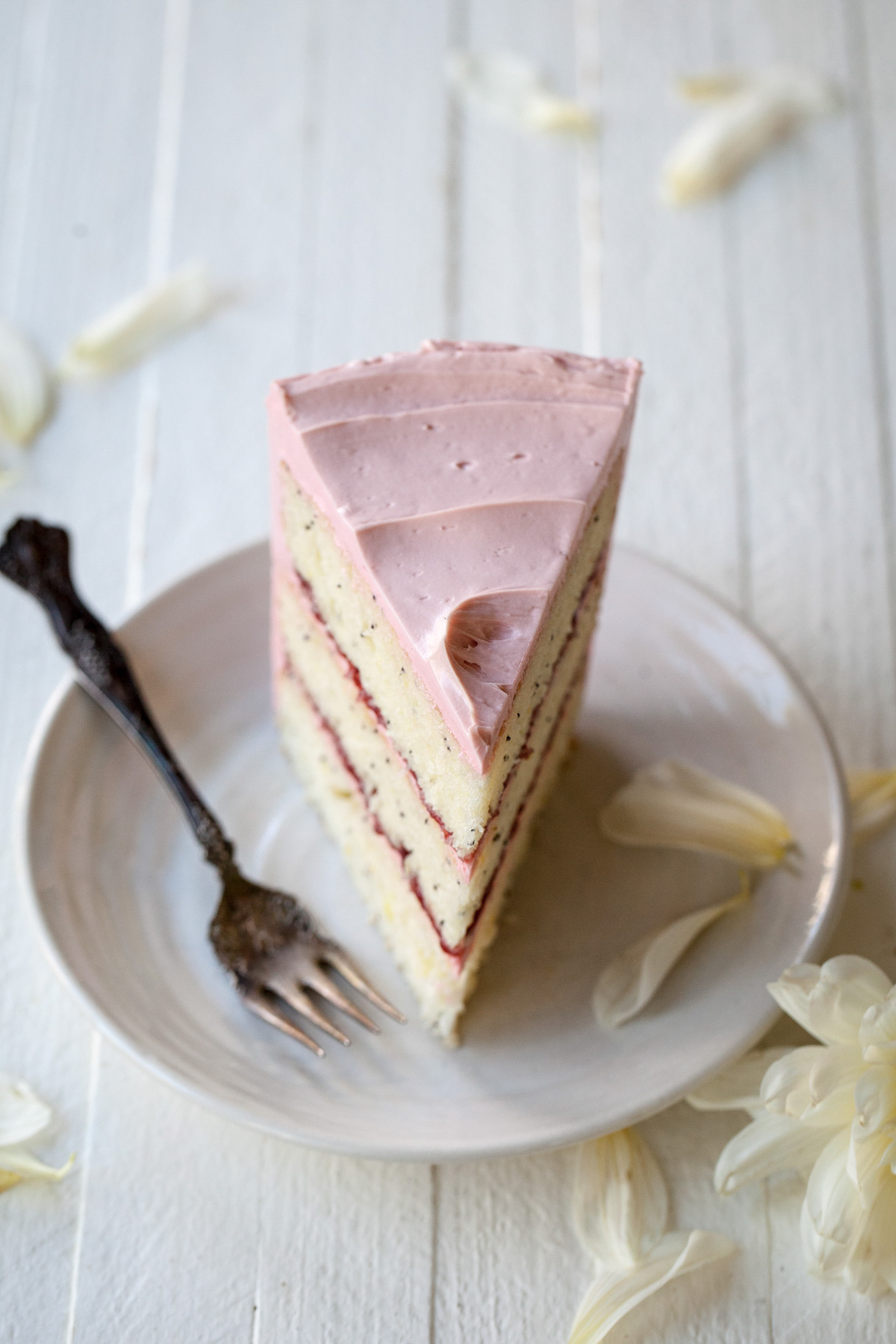 A slice of lemon poppy seed cake with raspberry jam and pink French buttercream