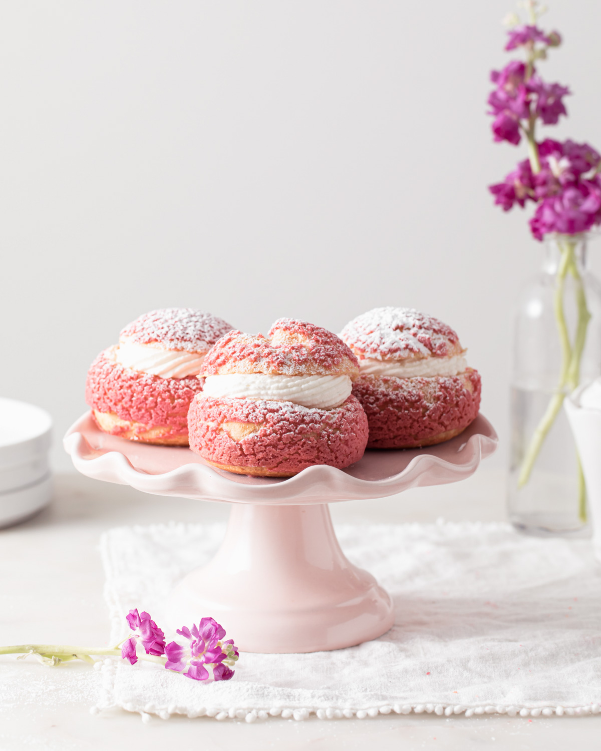 A pink cake stand with pink choux buns on top