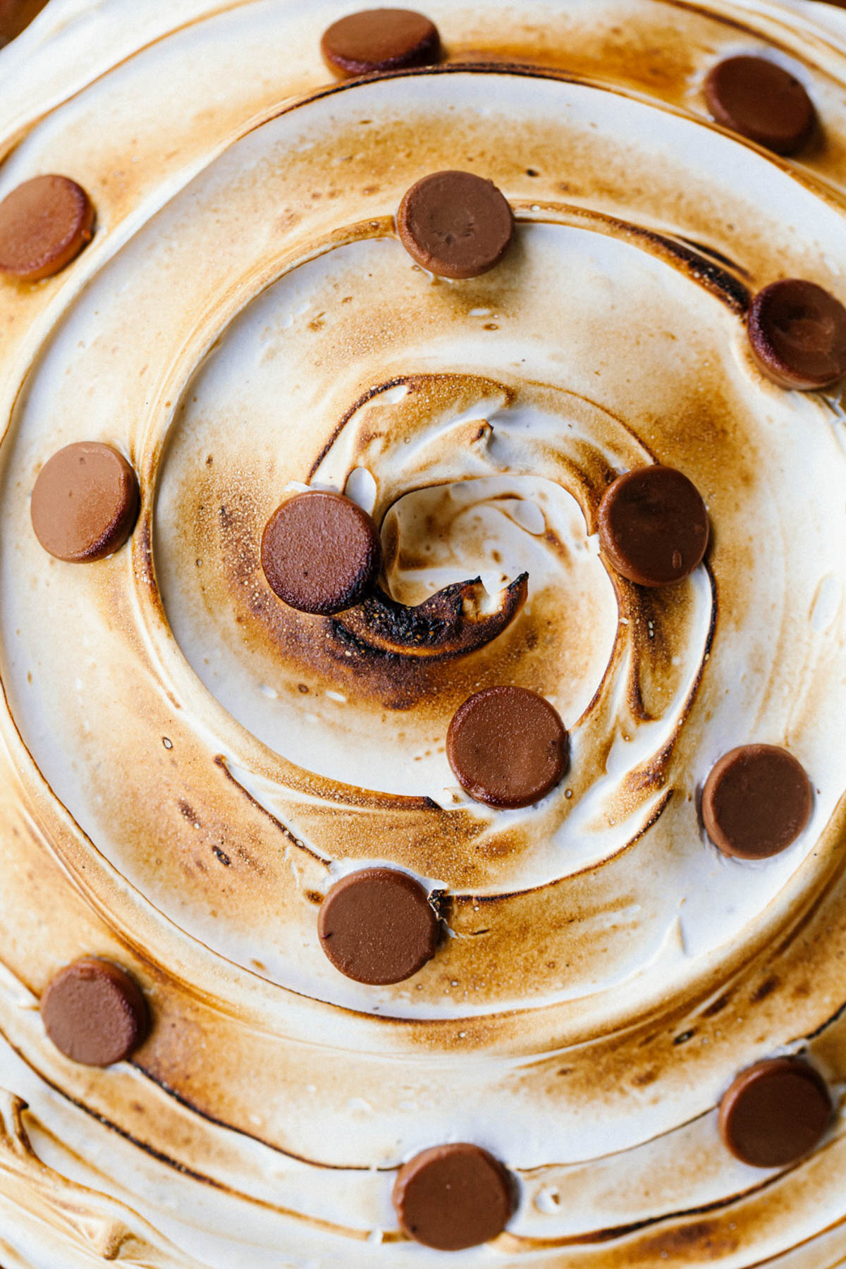 An overhead image of toasted meringue topping on a pie with chocolate chip polka dots