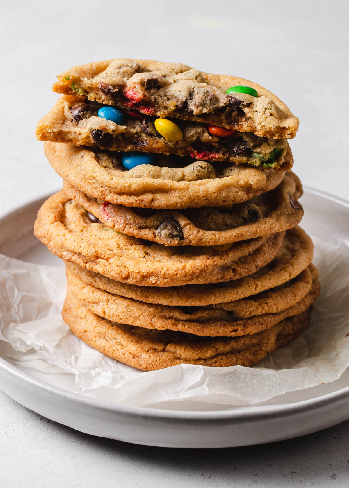 A stack of rainbow m and m crispy chocolate chip cookies on a plate