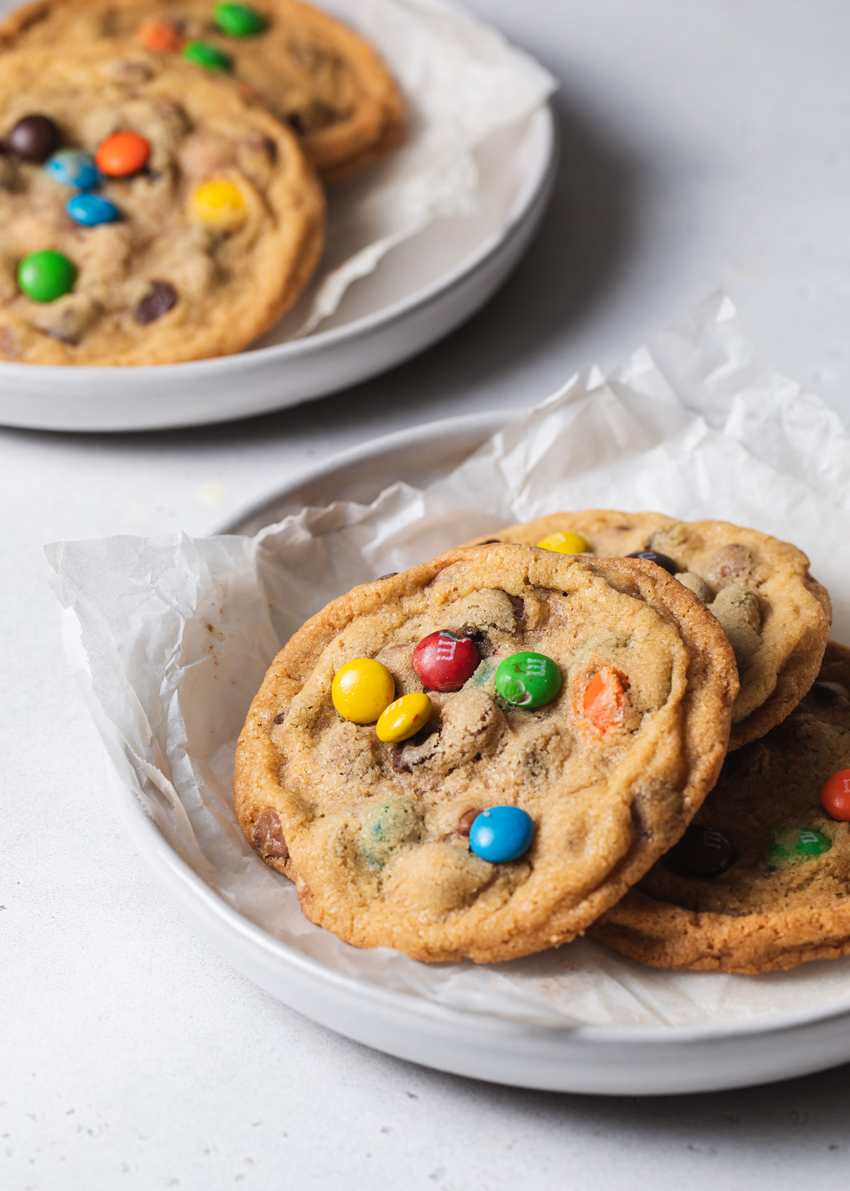 Two plates with a pile of rainbow and m chocolate chip cookies on top