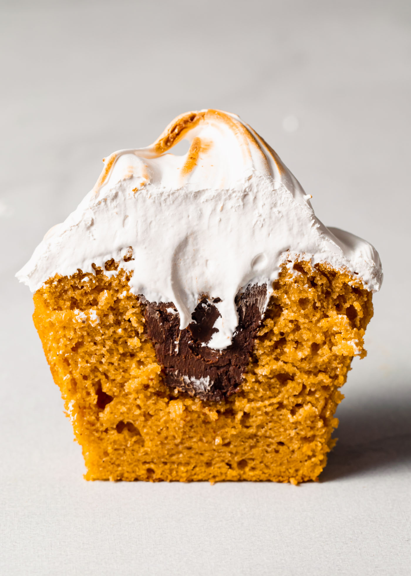 A pumpkin s'mores cupcake that has been sliced open to reveal the chocolate filling