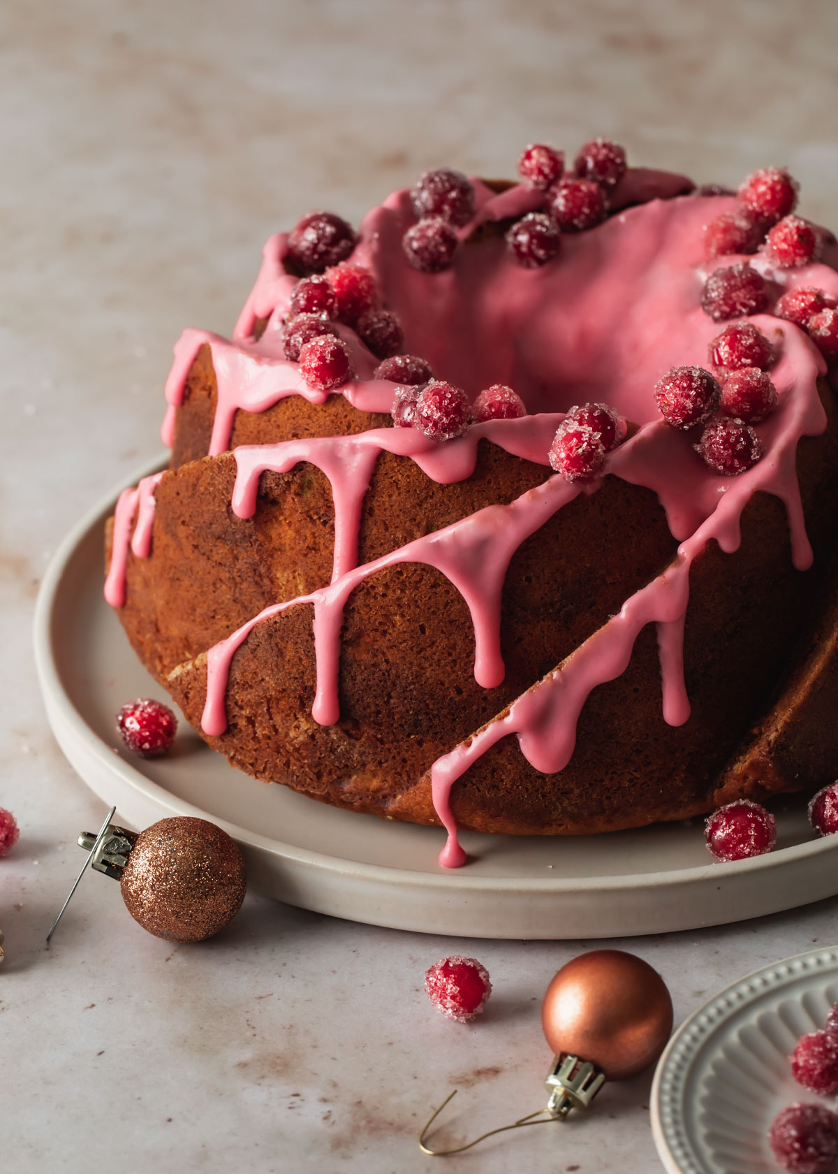 A cinnamon Bundt Cake on a platter with glaze and sugared cranberries on top