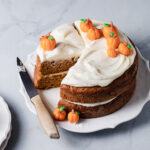 A maple pumpkin cake with swirls of maple cream cheese frosting and marzipan pumpkins on top.