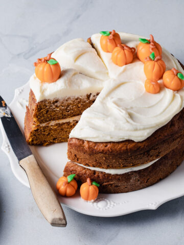 A maple pumpkin cake with swirls of maple cream cheese frosting and marzipan pumpkins on top.