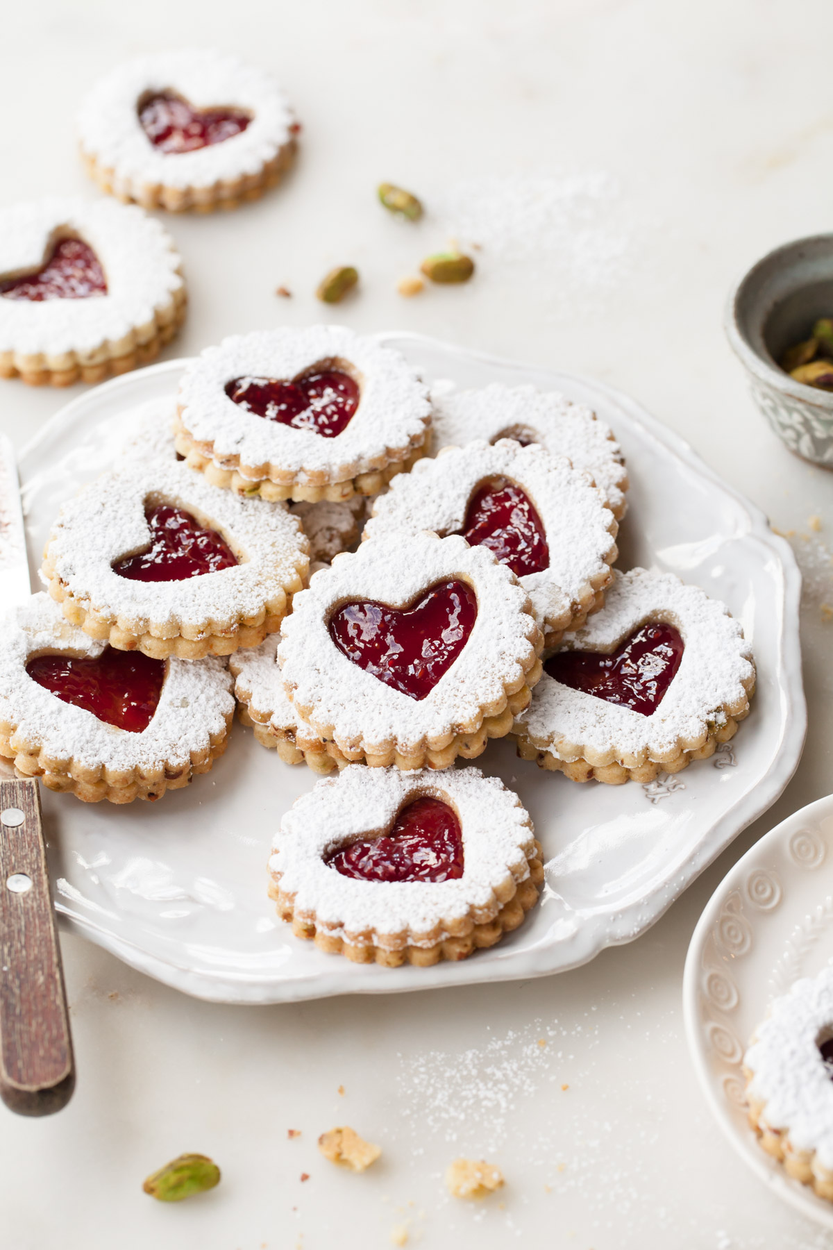 A plate full of pistachio liner cookies with raspberry jam centers