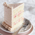 A slice of three-layer Rhubarb Ginger Cake with pink rhubarb buttercream frosting