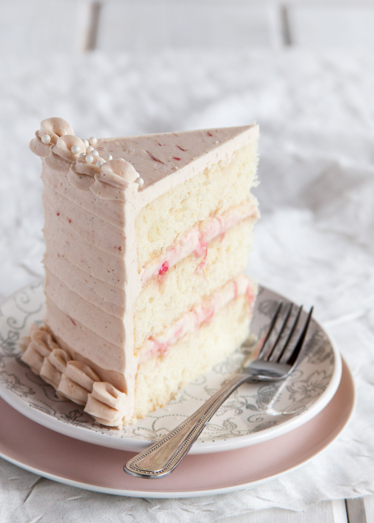 A slice of three-layer ginger cake with poached rhubarb filling and pink frosting.