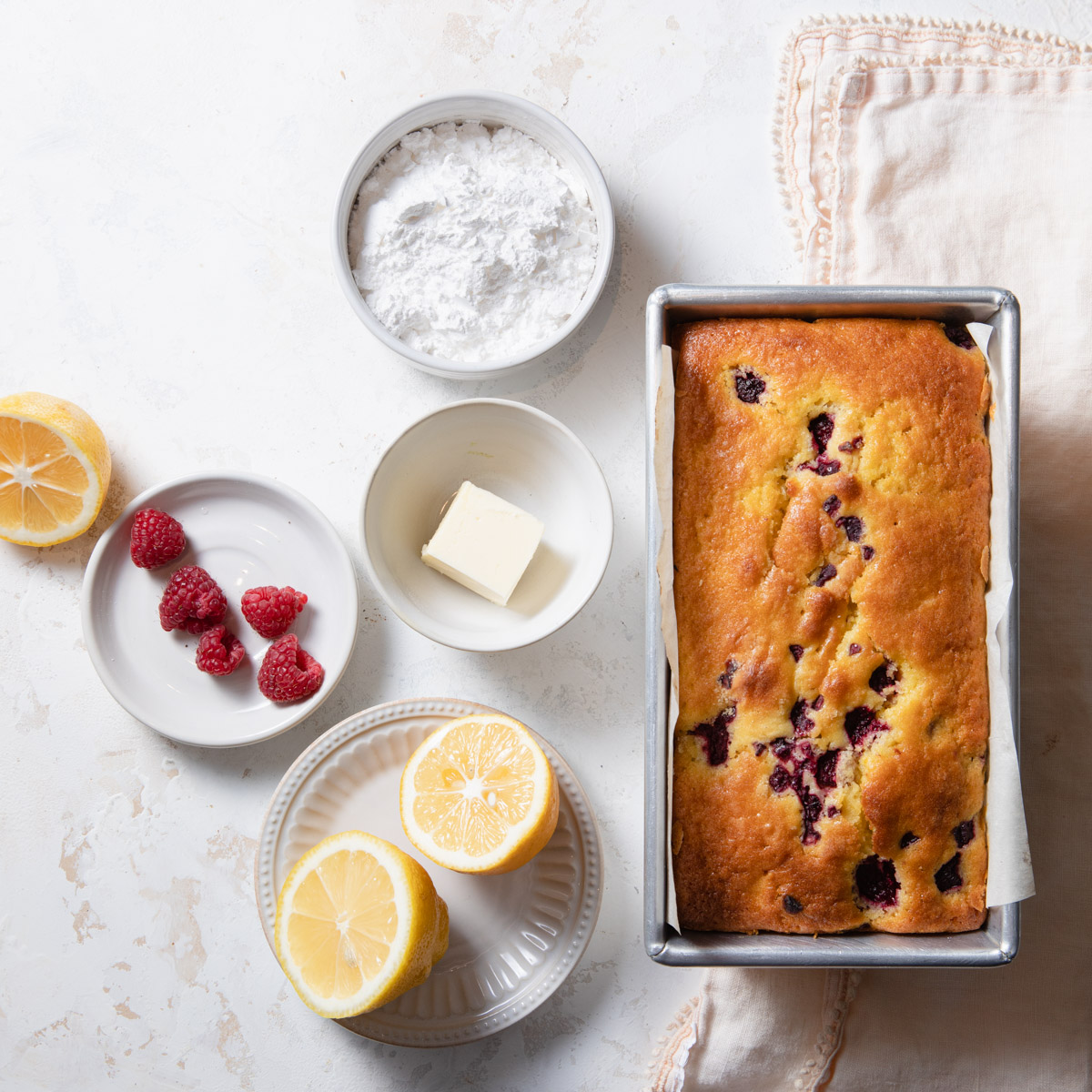 A baked raspberry lemon loaf cake with ingredients set aside for a lemon glaze