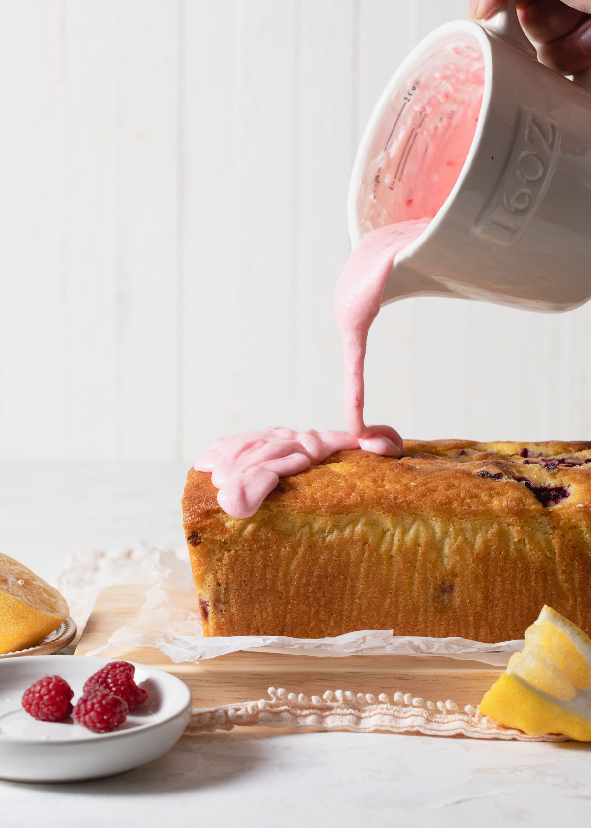 Pouring lemon raspberry glaze on top of lemon bread with raspberries