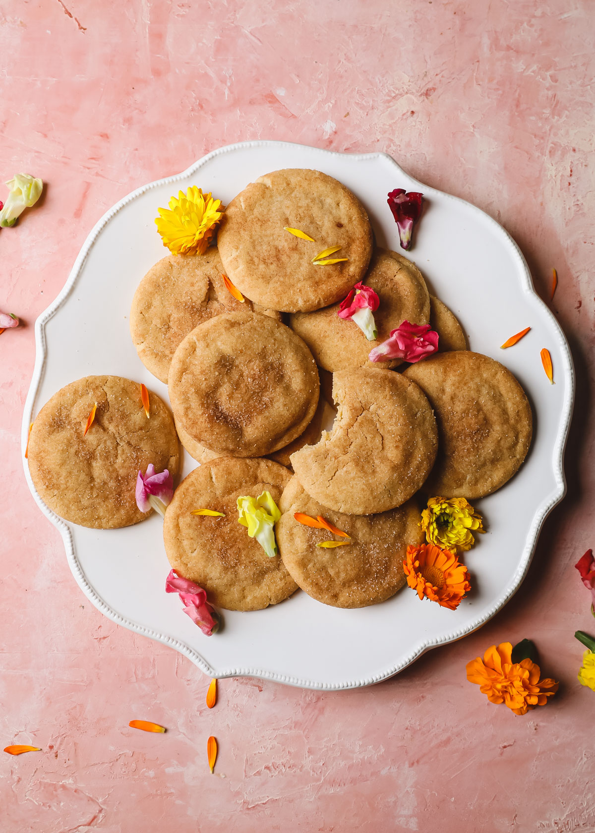 A platter of brown butter snickerdoodles with a sprinkle of edible flowers on a pink backdrop