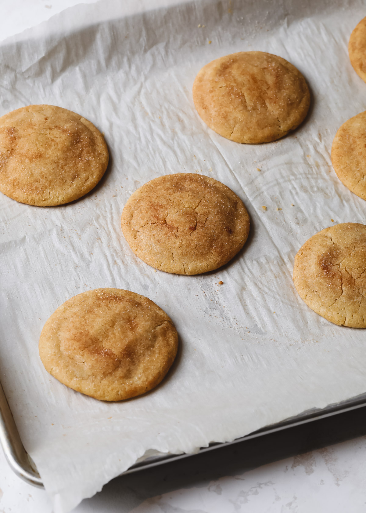 Freshly baked cookies coated in cinnamon sugar on a rimmed cookie sheet