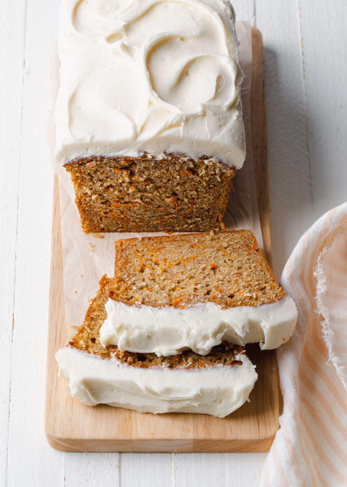 A sliced carrot cake loaf with cream cheese frosting on a wooden cutting board