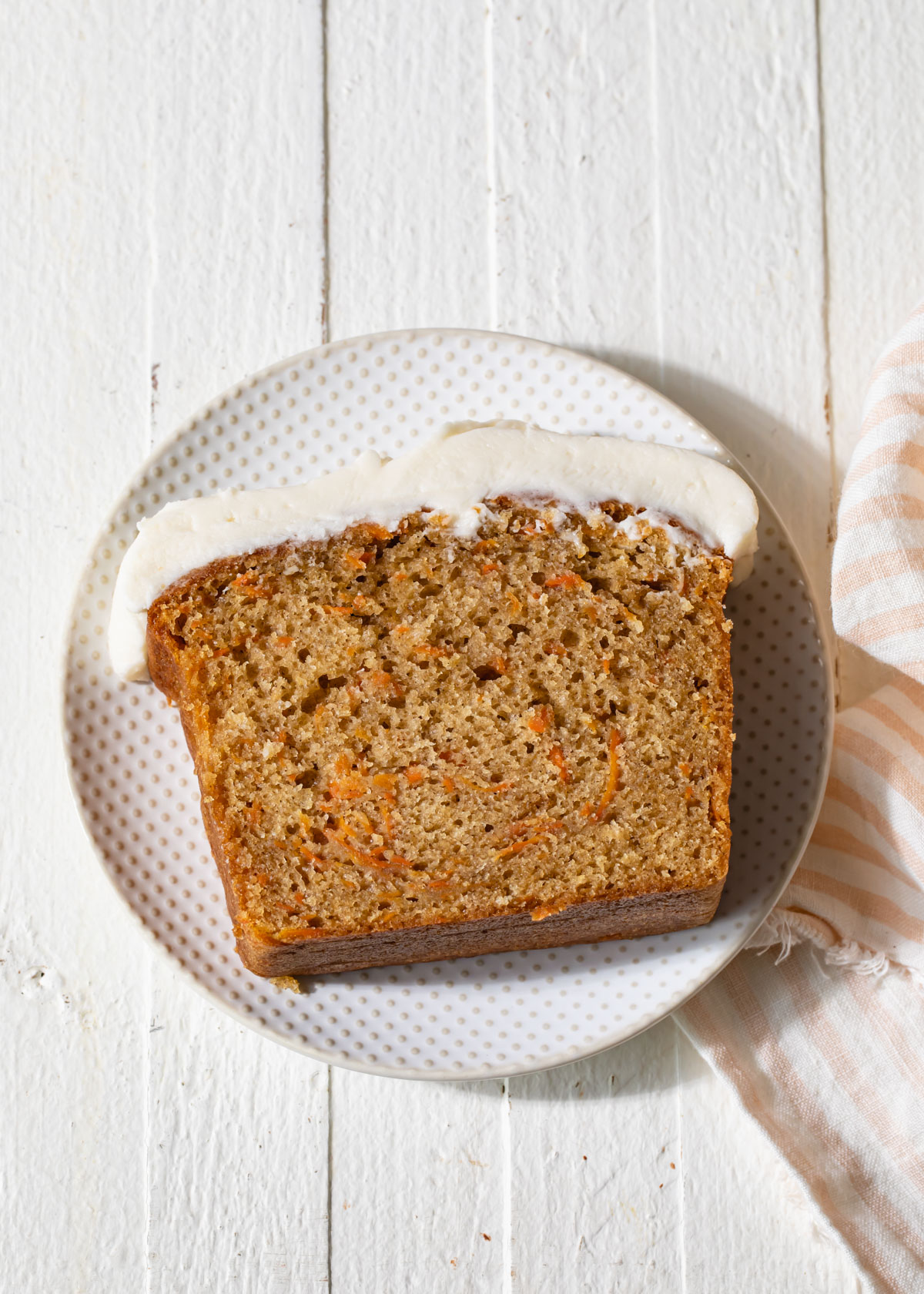 A thick slice of carrot cake on a white plate with cream cheese frosting