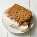 A thick slice of carrot cake on a white plate with a fork taking a bite