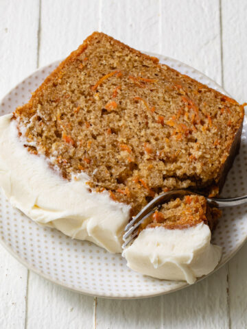 A thick slice of carrot cake on a white plate with a fork taking a bite