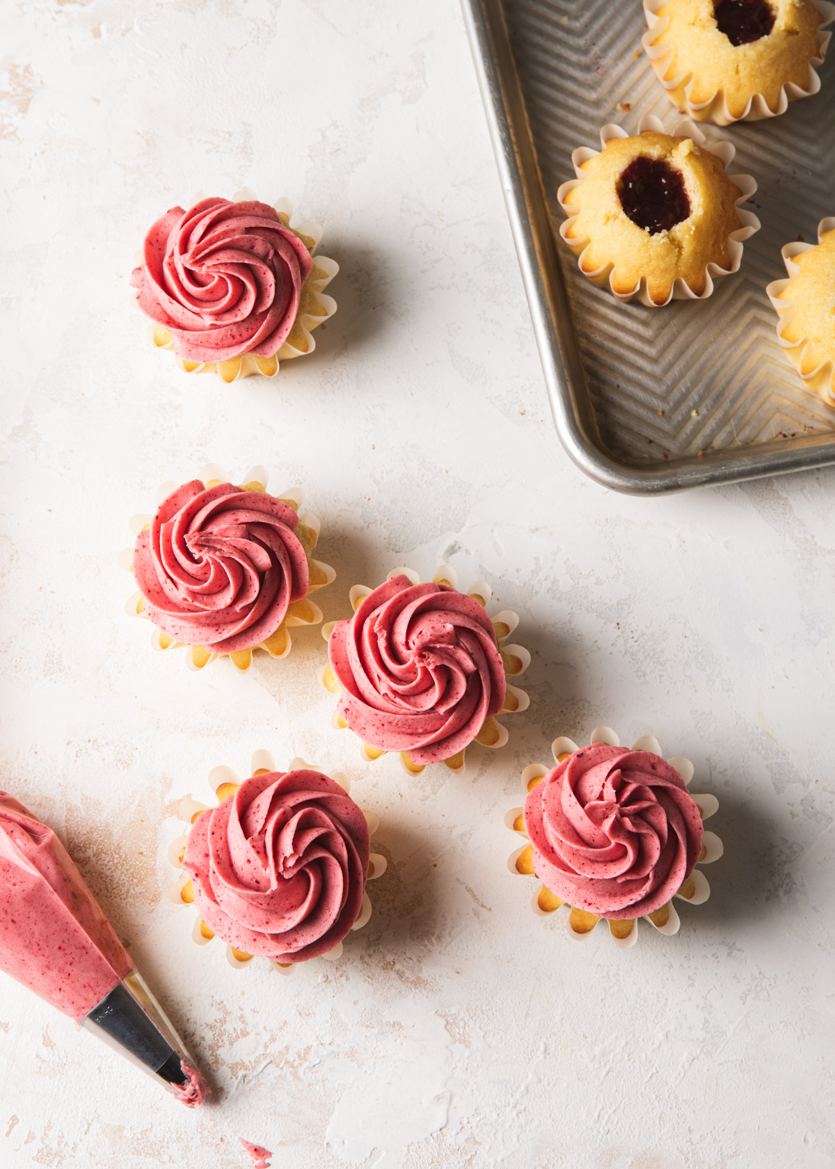 Filling and frosting raspberry cupcakes with buttercream and jam