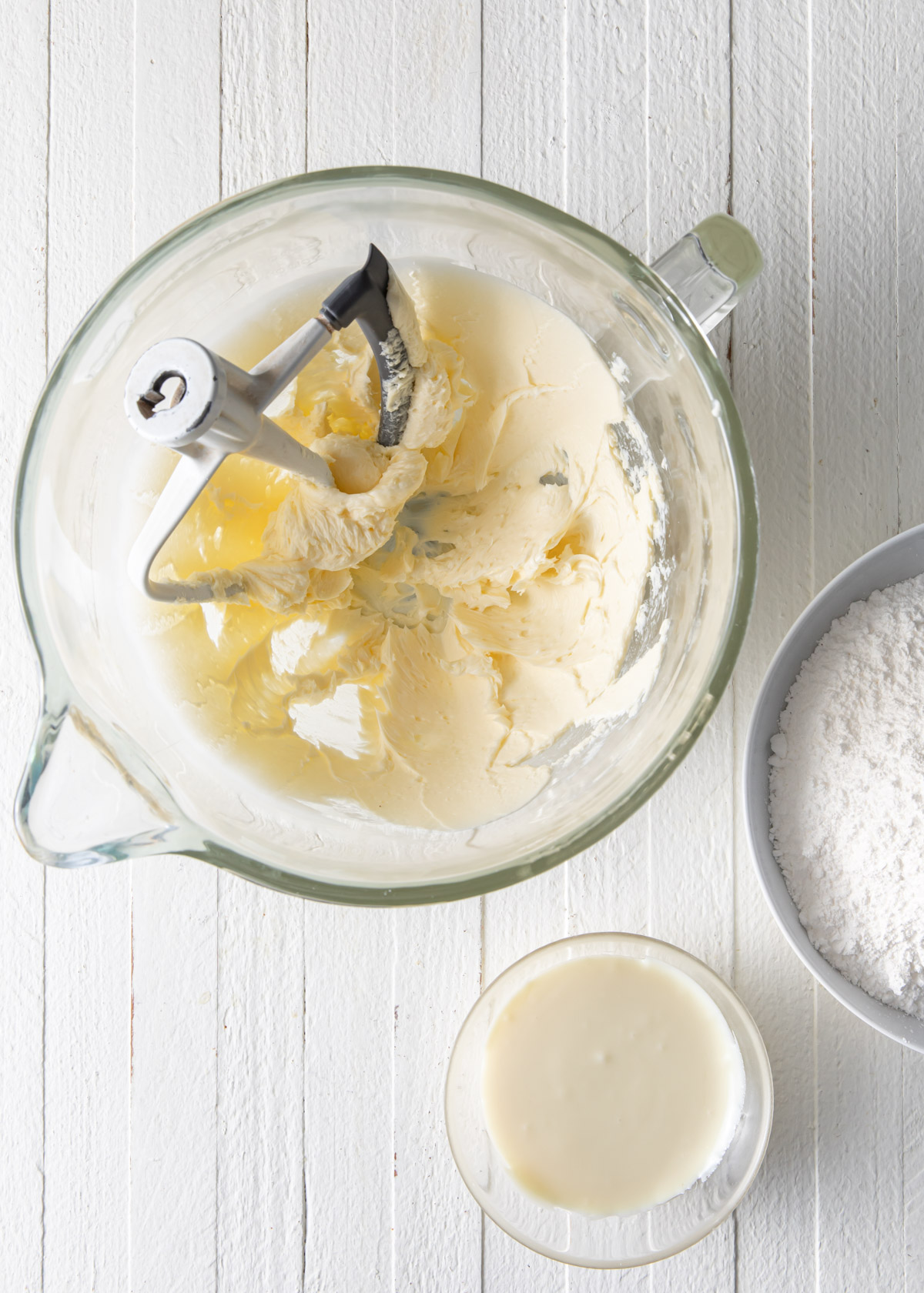 A mixing bowl with creamy butter and other ingredients to make white chocolate frosting