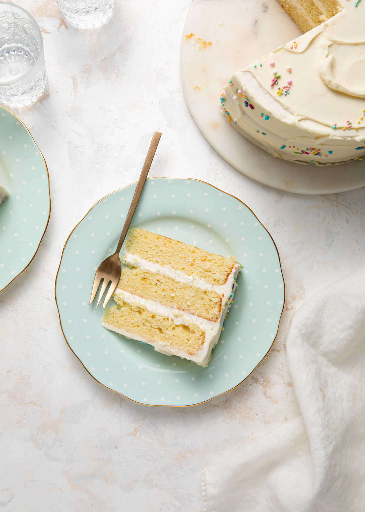 A turquoise plate with a slice of yellow cake and buttercream frosting
