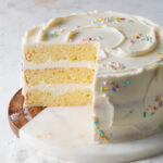 A sliced open three layer, yellow 8 inch cake with white chocolate icing