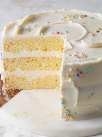 A sliced open three layer, yellow 8 inch cake with white chocolate icing