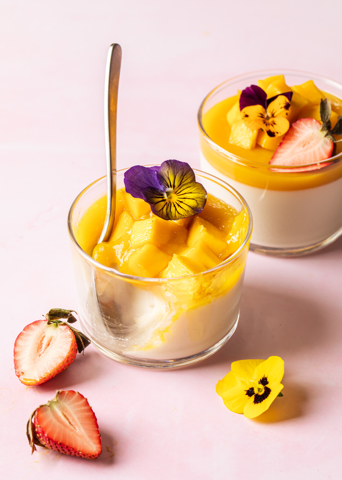 Two glass dishes filled with mango panna cotta with edible flowers and strawberries on top