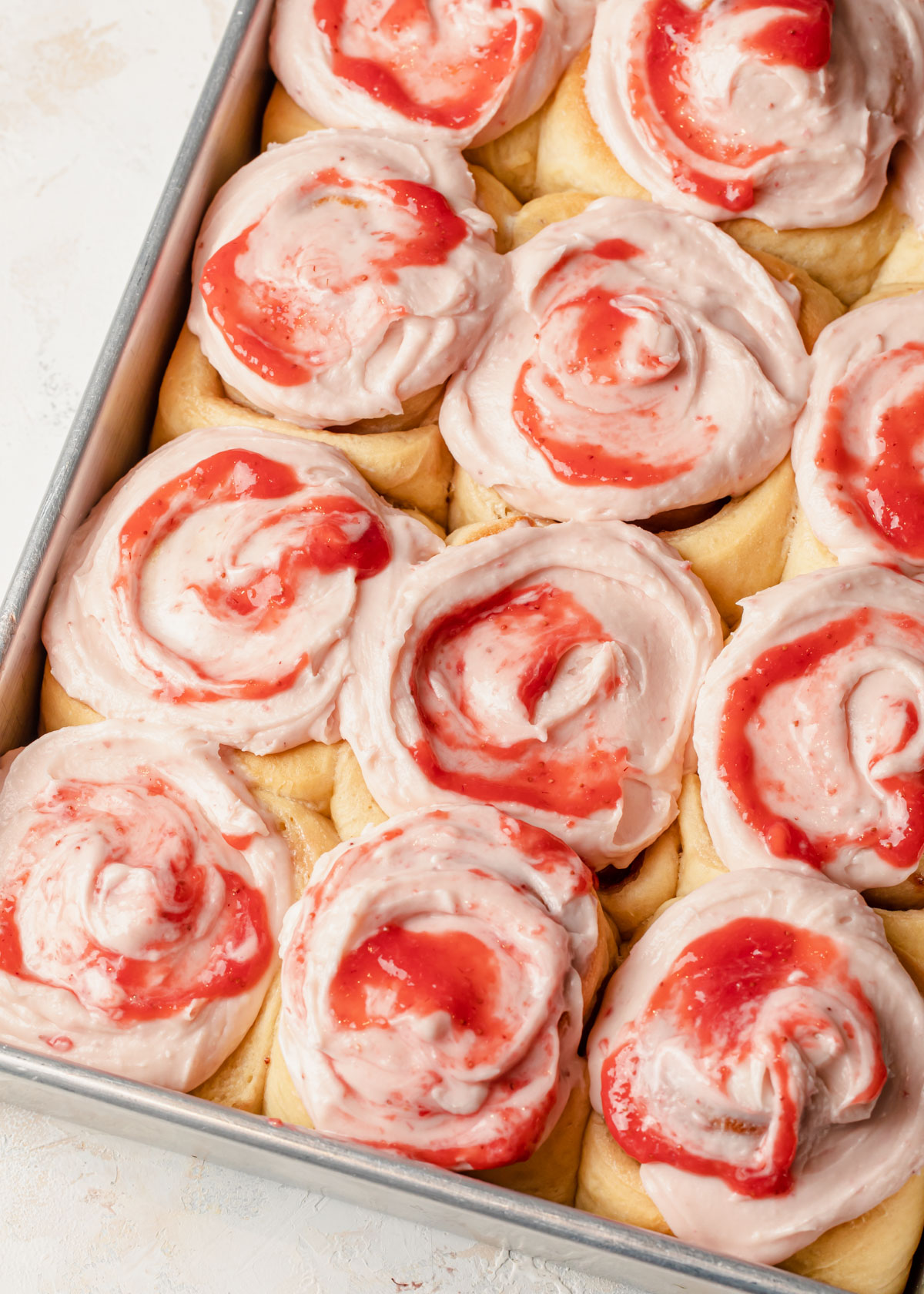A baking tray full of baked jam rolls with strawberry cream cheese and jam topping