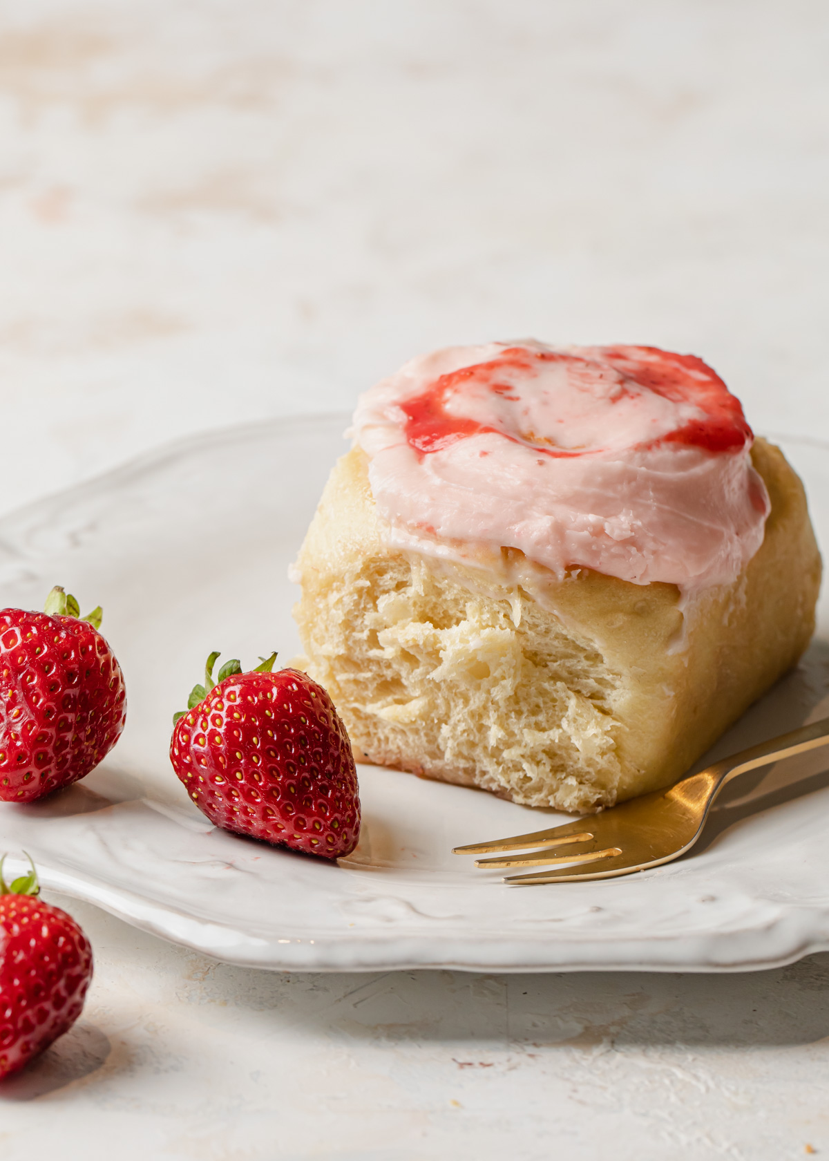 A cinnamon roll with strawberry cream cheese frosting on top and jam filling on a plate