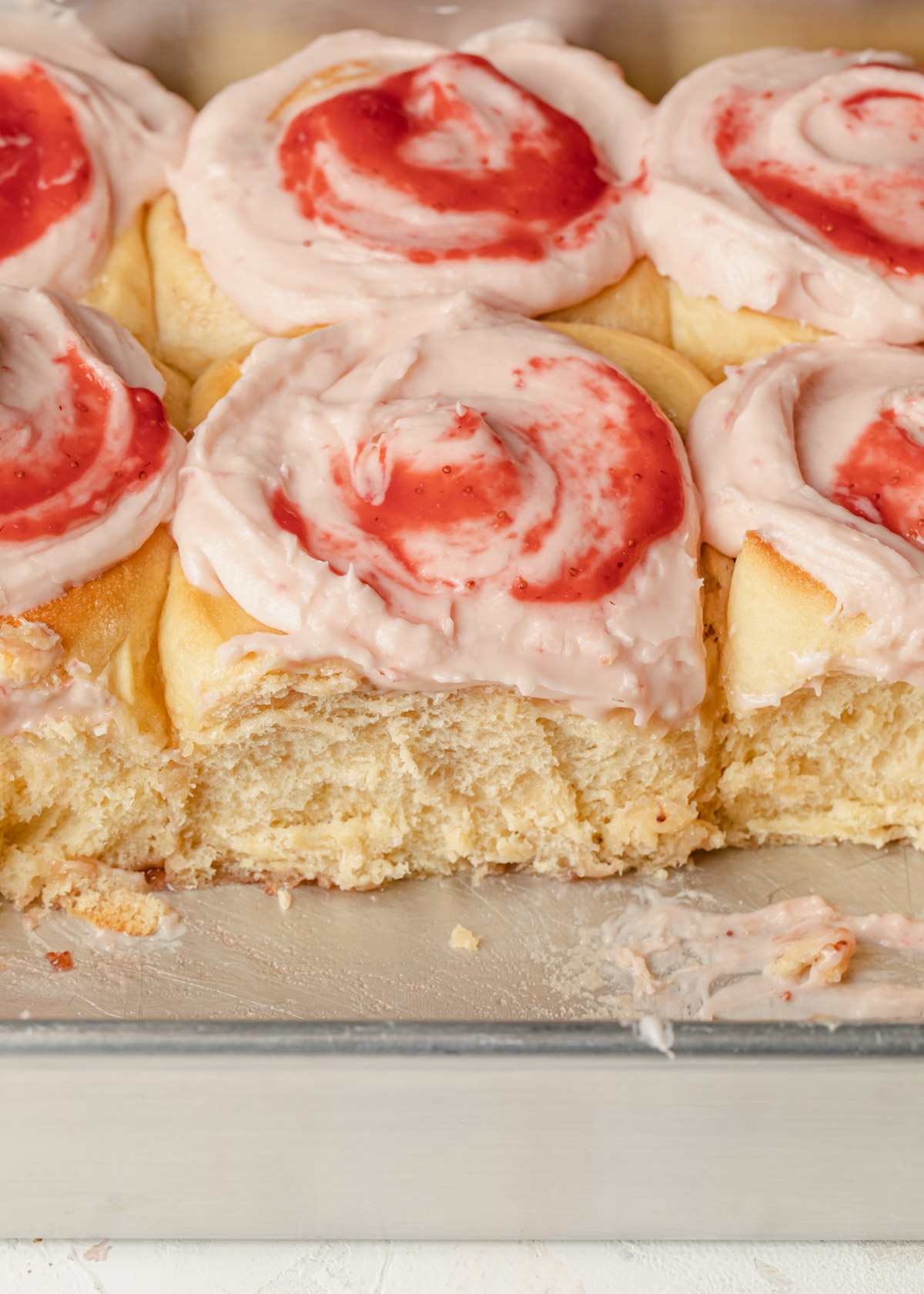 Strawberry cinnamon rolls that are frosted in the pan and showing off the fluffy texture of the dough.