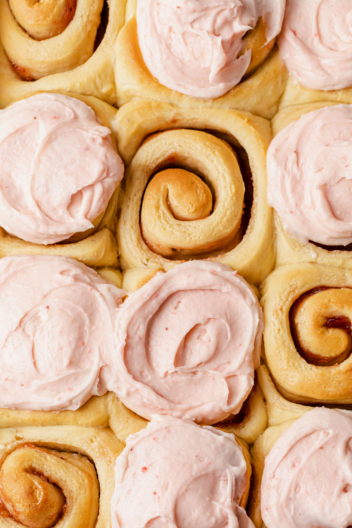 A close-up of jam rolls being frosted with strawberry cream cheese
