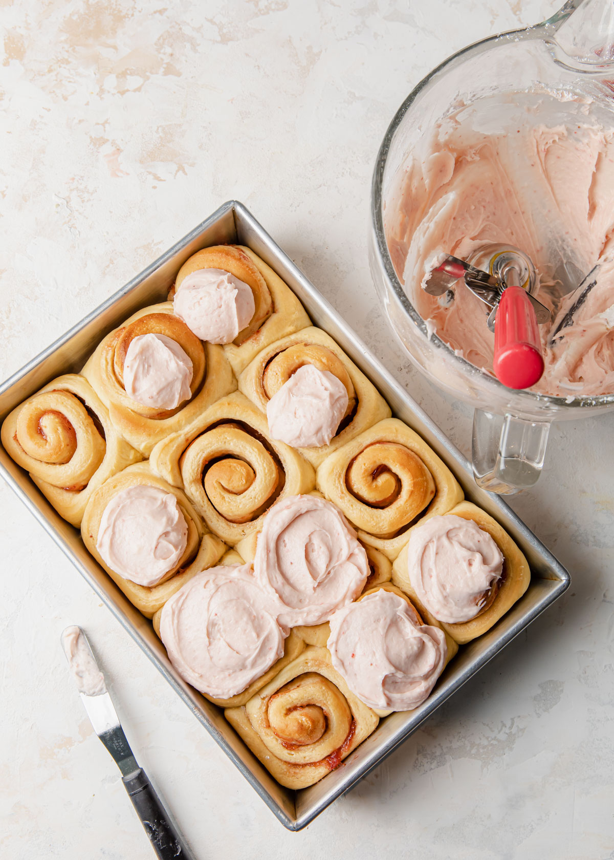 Adding strawberry cream cheese frosting on top of baked cinnamon rolls