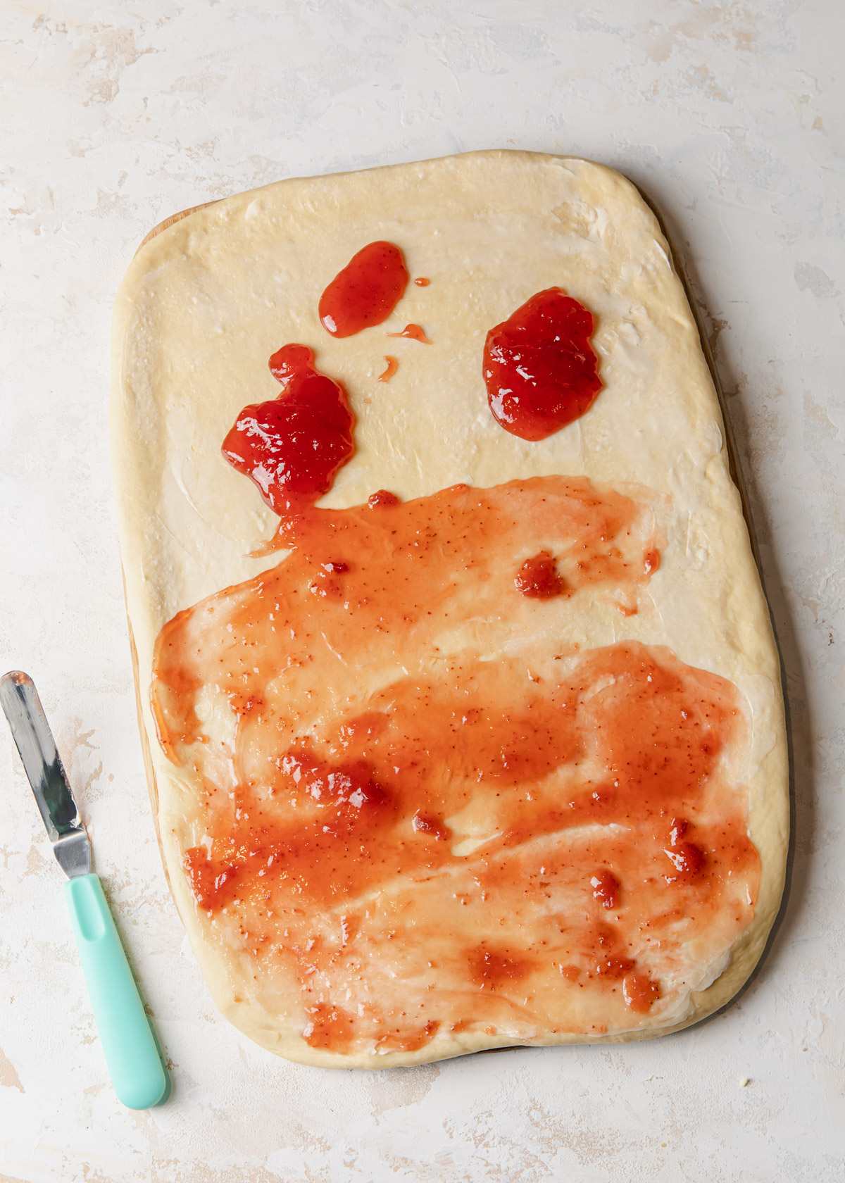 Spreading jam for cinnamon roll filling on rolled out dough