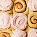 A close-up of jam rolls being frosted with strawberry cream cheese