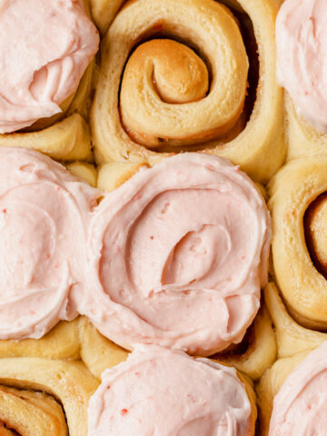 A close-up of jam rolls being frosted with strawberry cream cheese