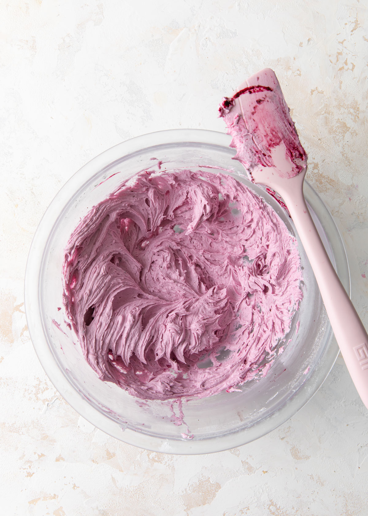 A bowl of fluffy blueberry buttercream on a white table