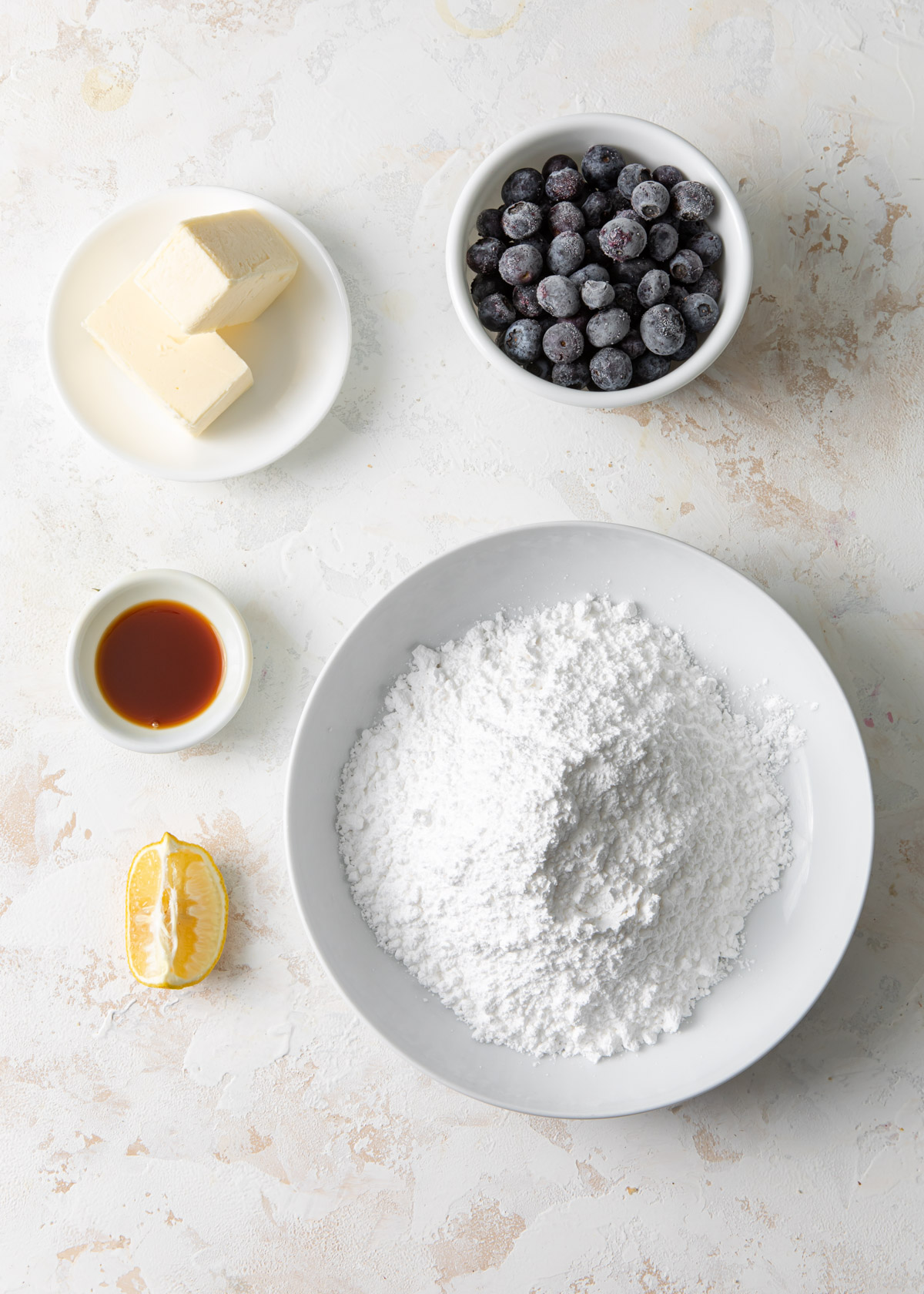 The ingredients for blueberry buttercream set out in bowl on top of a white table