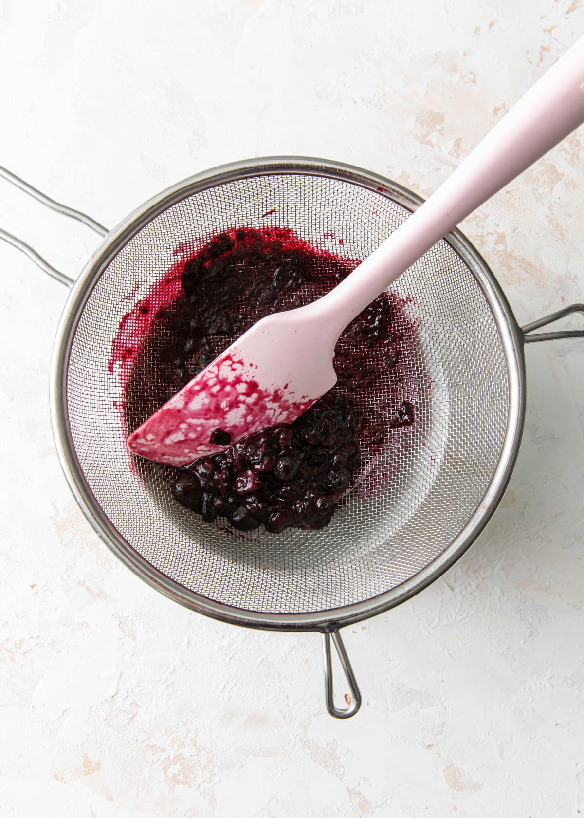 Straining blueberry sauce through a mesh sieve